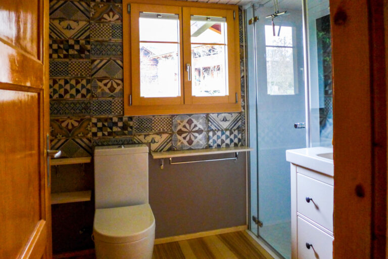 Blick ins Bad mit weißem Lavabo und Toilettensitz vor blau, grau, braun gemusterter Wand