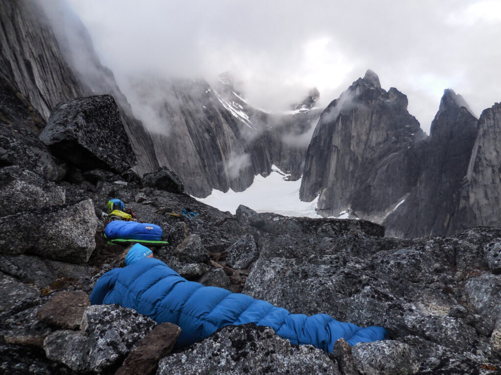 Zwei Menschen schlafen in blauen Schlafsäcken mit Bergen und Schnee als Kulisse
